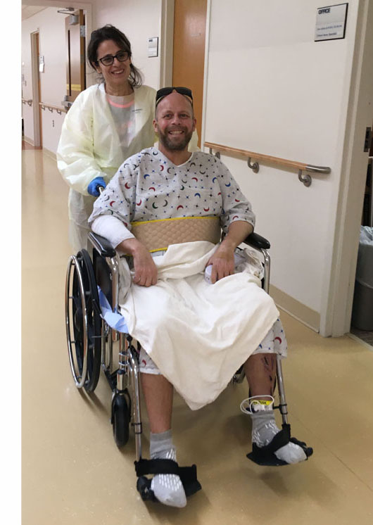 Jomania is pushing Paul in a wheelchair, both of them smiling or laughing.  Paul is wearing his sunglasses on the top of his head.